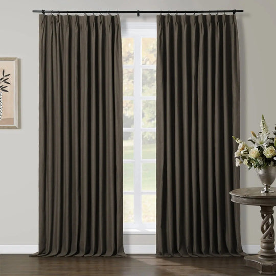 Two dark brown pleated window curtains in a modern room with a white-framed window, a minimalist botanical print, and an ornate twisted-base table with white and cream flowers