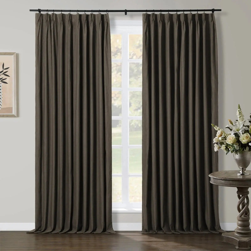Two dark brown pleated window curtains in a modern room with a white-framed window, a minimalist botanical print, and an ornate twisted-base table with white and cream flowers