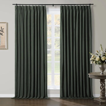 Dark green pinch-pleat curtains adorning a sunlit window in a contemporary room, featuring a carved wooden side table with a white flower arrangement and minimalist wall art