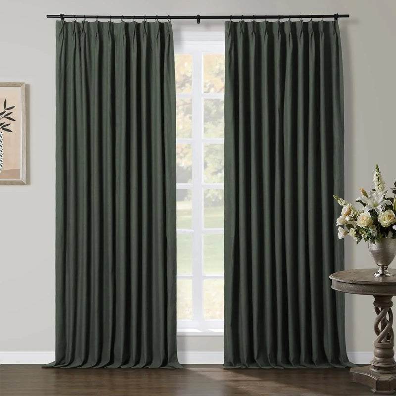 Dark green pinch-pleat curtains adorning a sunlit window in a contemporary room, featuring a carved wooden side table with a white flower arrangement and minimalist wall art