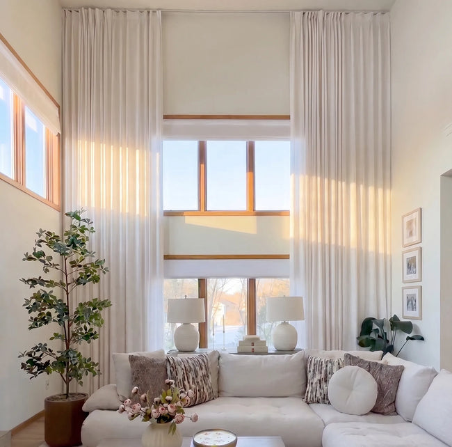 Modern living room with white sofa, decorative pillows, and large windows with extra long curtains.