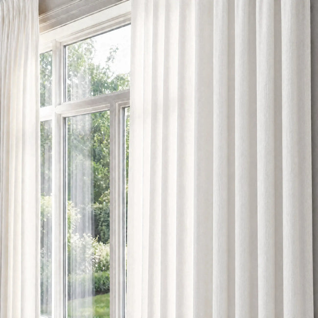 White curtains hanging in front of a window with a view of greenery outside.