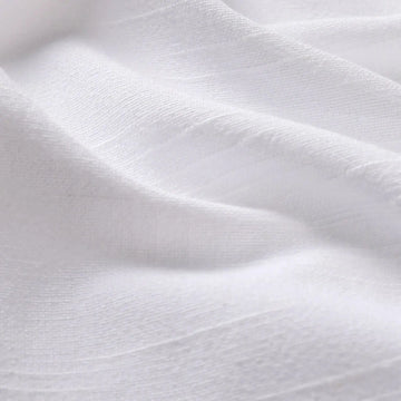 Close-up photograph of white textured fabric displaying gentle folds subtle shadows and a fine linen-like weave