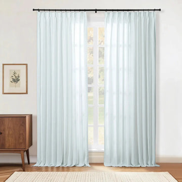 Light blue sheer curtains covering a window in a modern room, featuring a black curtain rod, a wooden mid-century cabinet with a framed botanical print, and a beige textured rug on a hardwood floor