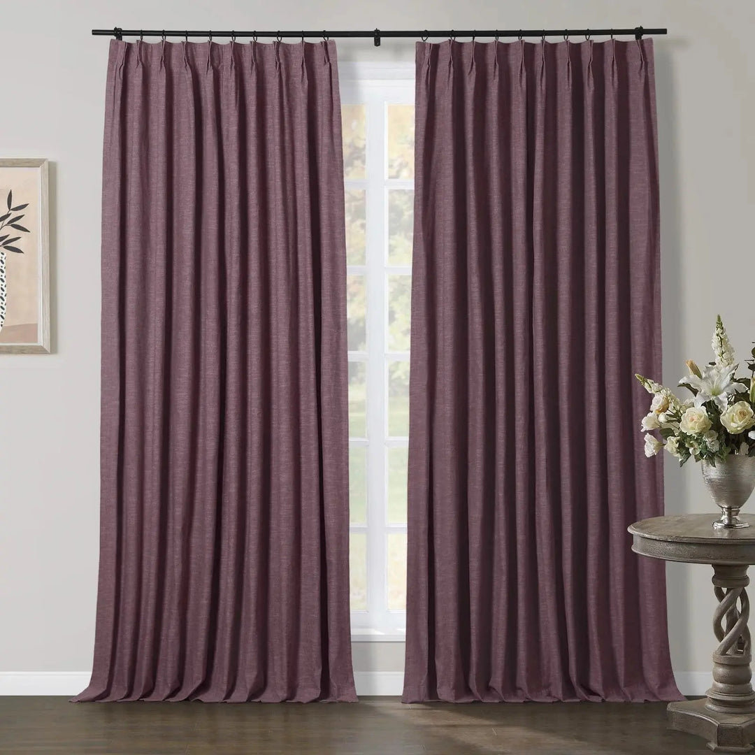 Textured plum pinch pleat curtains on a black rod in an interior setting, featuring a carved wooden side table with white floral arrangement and minimalist framed artwork