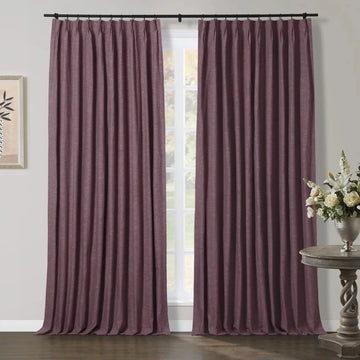 Textured plum pinch pleat curtains on a black rod in an interior setting, featuring a carved wooden side table with white floral arrangement and minimalist framed artwork