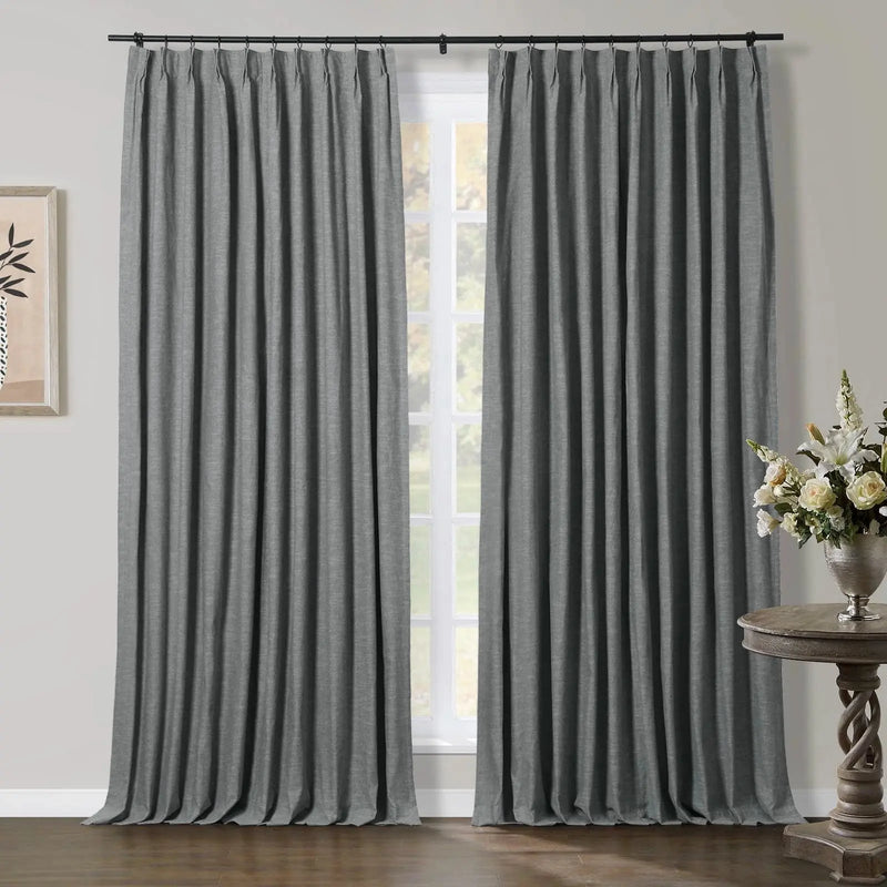 Charcoal gray pinch pleat linen blend curtains in an interior room with a rustic carved wood side table holding a white floral arrangement and minimalist framed art