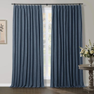 Dark blue pinch pleat curtains frame a multi-pane window in a room featuring a rustic wood side table with a silver vase of white flowers and a framed abstract plant artwork