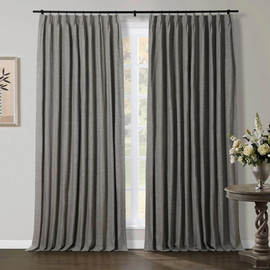 Grey pleated curtains hang from a black rod over a window, flanked by abstract wall art and a silver vase with a white floral arrangement on a carved wooden table