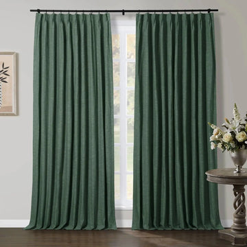 Dark green textured pinch pleat curtains hanging from a black rod in an interior room featuring a carved wooden side table with a white and cream floral arrangement and framed minimalist art