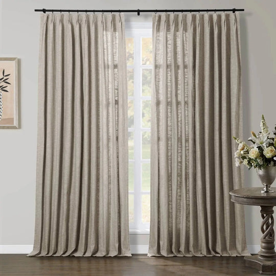Beige textured linen blend pinch pleat curtains on a black rod in a room featuring a bouquet of white roses and lilies in a silver vase on a carved wooden side table and framed minimalist botanical art