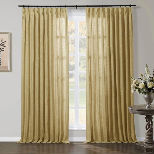 A pair of pleated, textured gold curtains framing a sunlit window in a living room, accompanied by a rustic carved wood side table adorned with white roses and lilies in a silver vase, and a framed abstract artwork on the left wall
