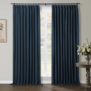 Photography of an interior room featuring elegant dark blue pinch-pleat curtains framing a window that looks out onto a green outdoor landscape, with a decorative wooden console table holding a silver vase of white and yellow flowers