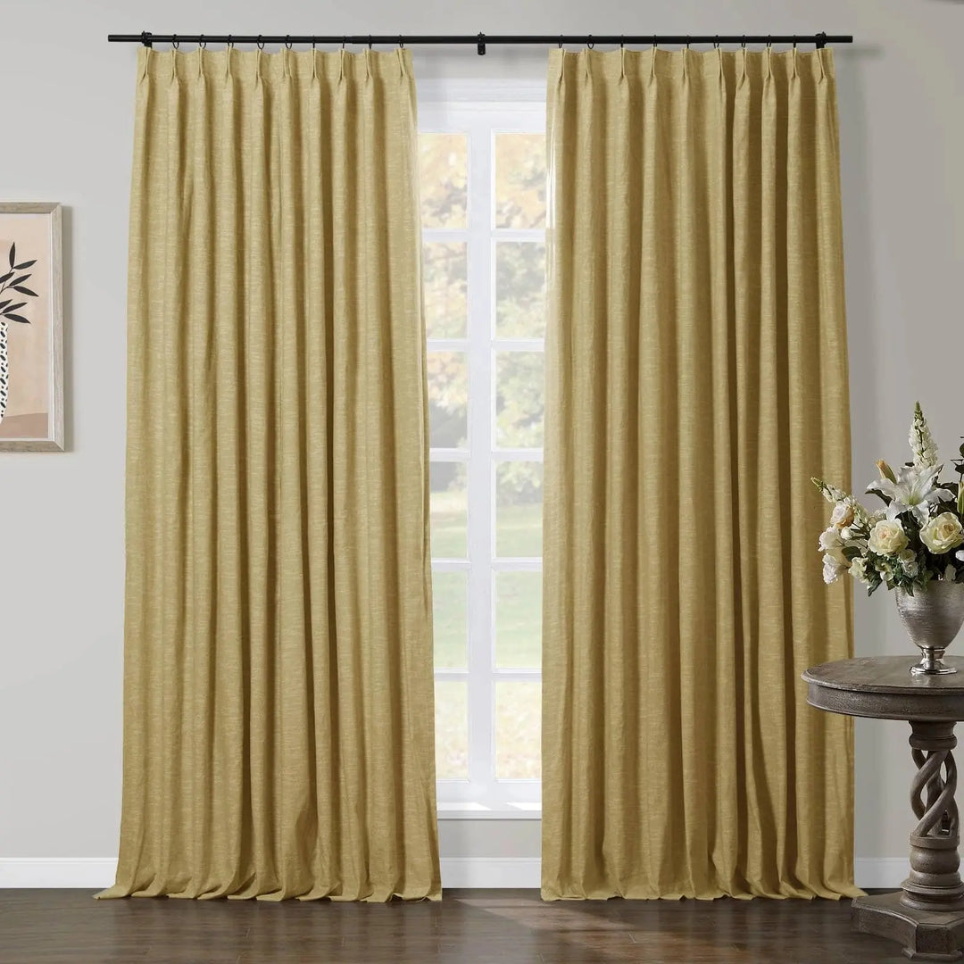 Textured gold curtains framing a window in a room, with a black curtain rod, a rustic carved wooden accent table, and a silver vase of white flowers