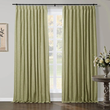 Light green linen-textured curtains hung on a black rod framing a window in a room, with a twisted wooden accent table holding a silver vase of white lilies and cream roses